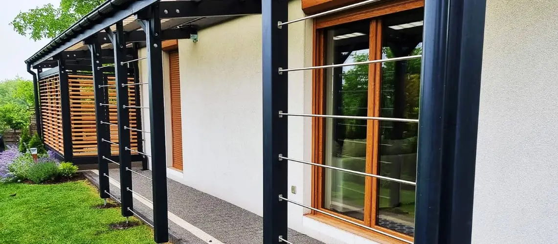 Narożne zadaszenie tarasu w kształcie litery L wyposażone w przesuwne drzwi z żaluzjami typu Shutters